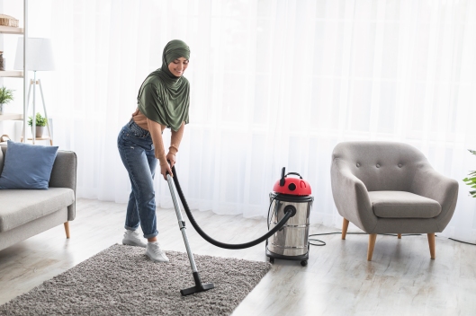 Cheerful muslim woman cleaning rug carpet with vacuum cleaner